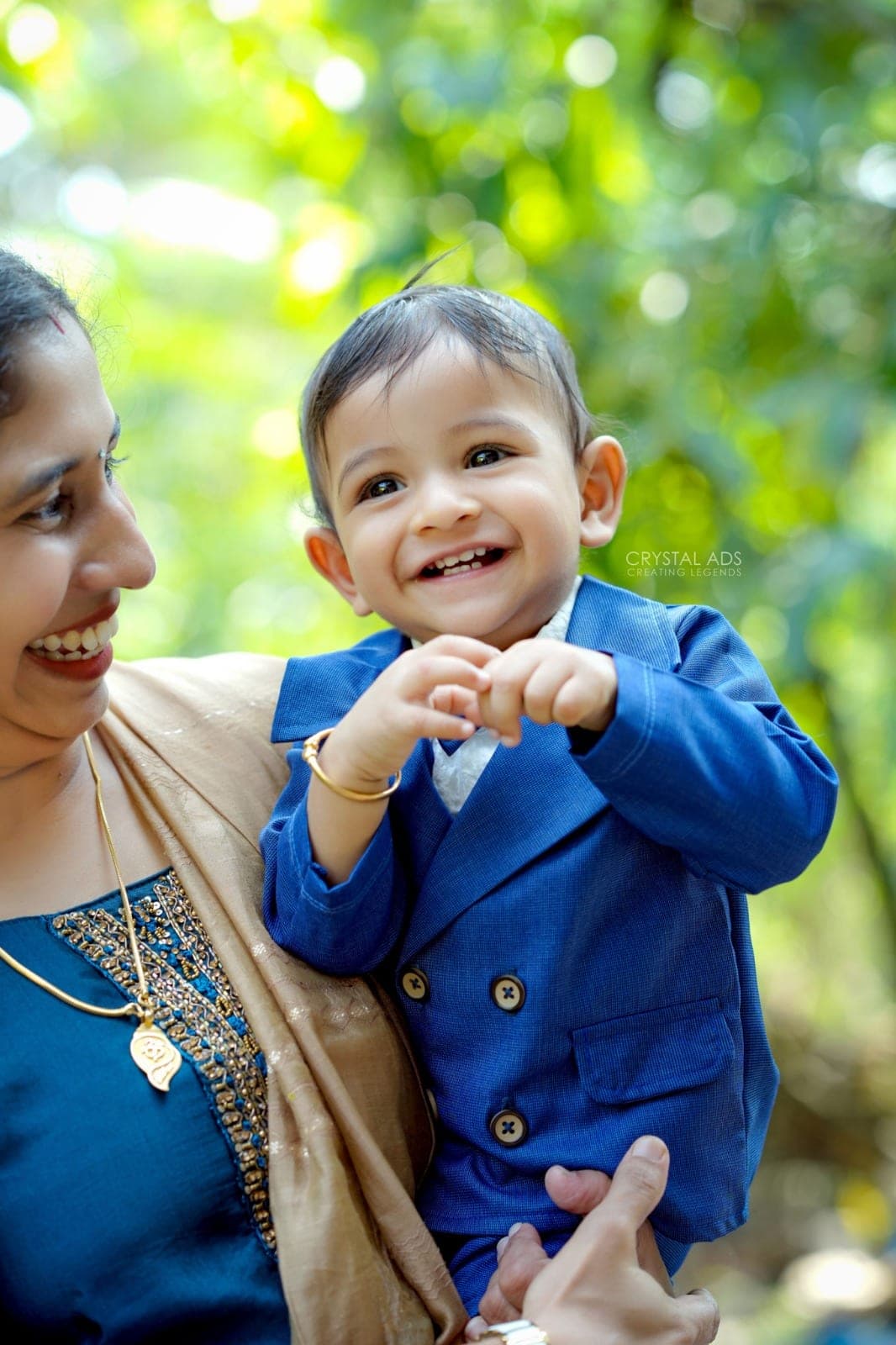 Smiling baby boy in a blue suit held up by his mother