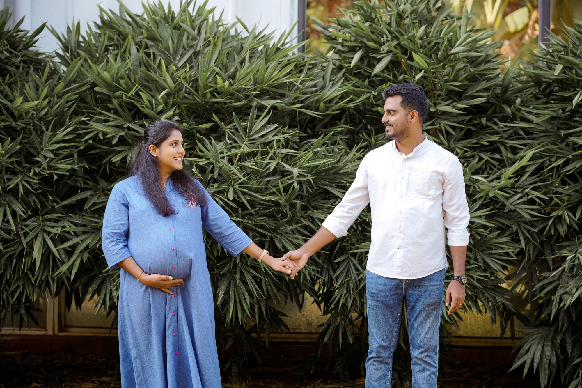 Expecting couple holding hands in front of greenery