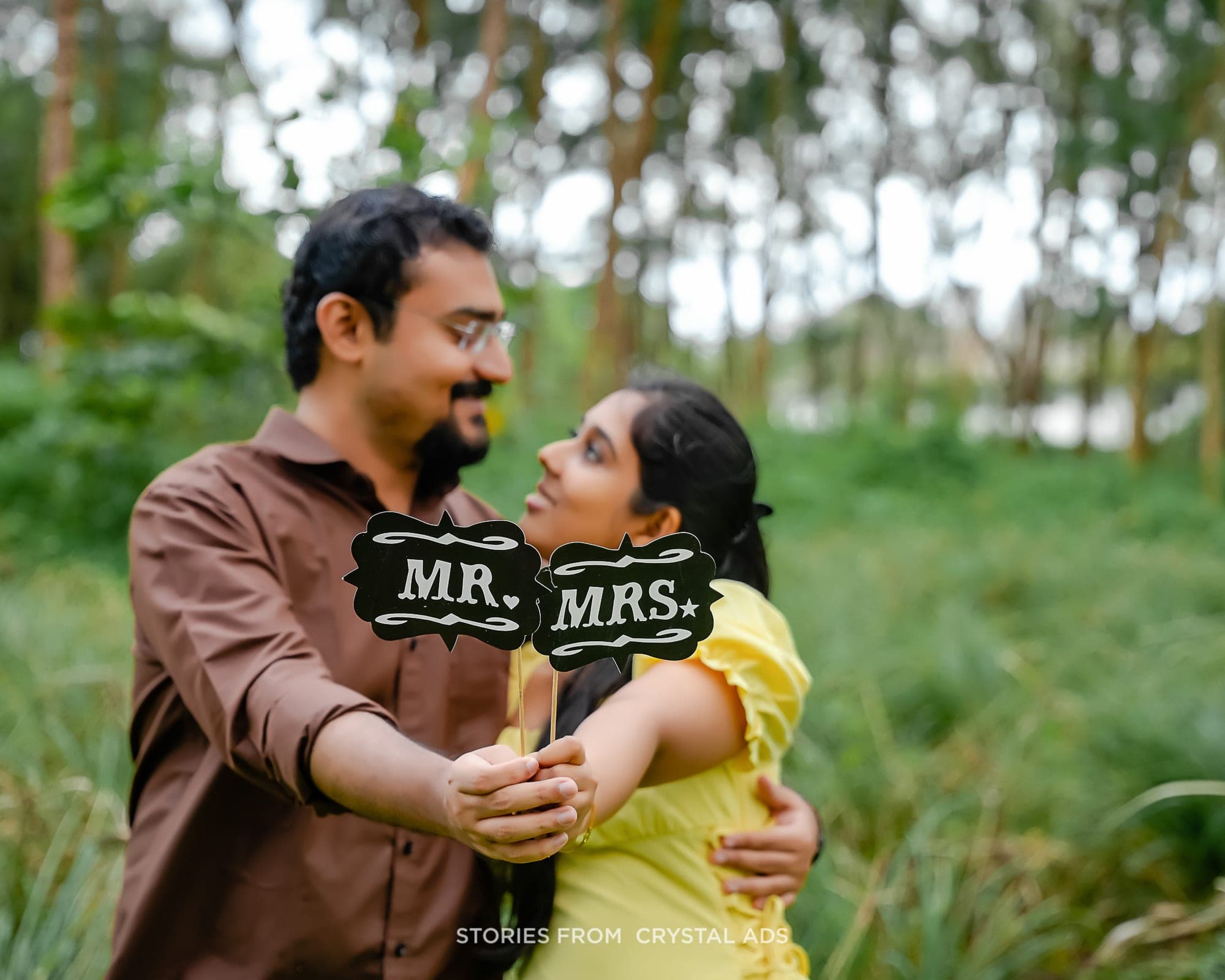 Couple laughing together in a forest, holding "Mr." and "Mrs." signs
