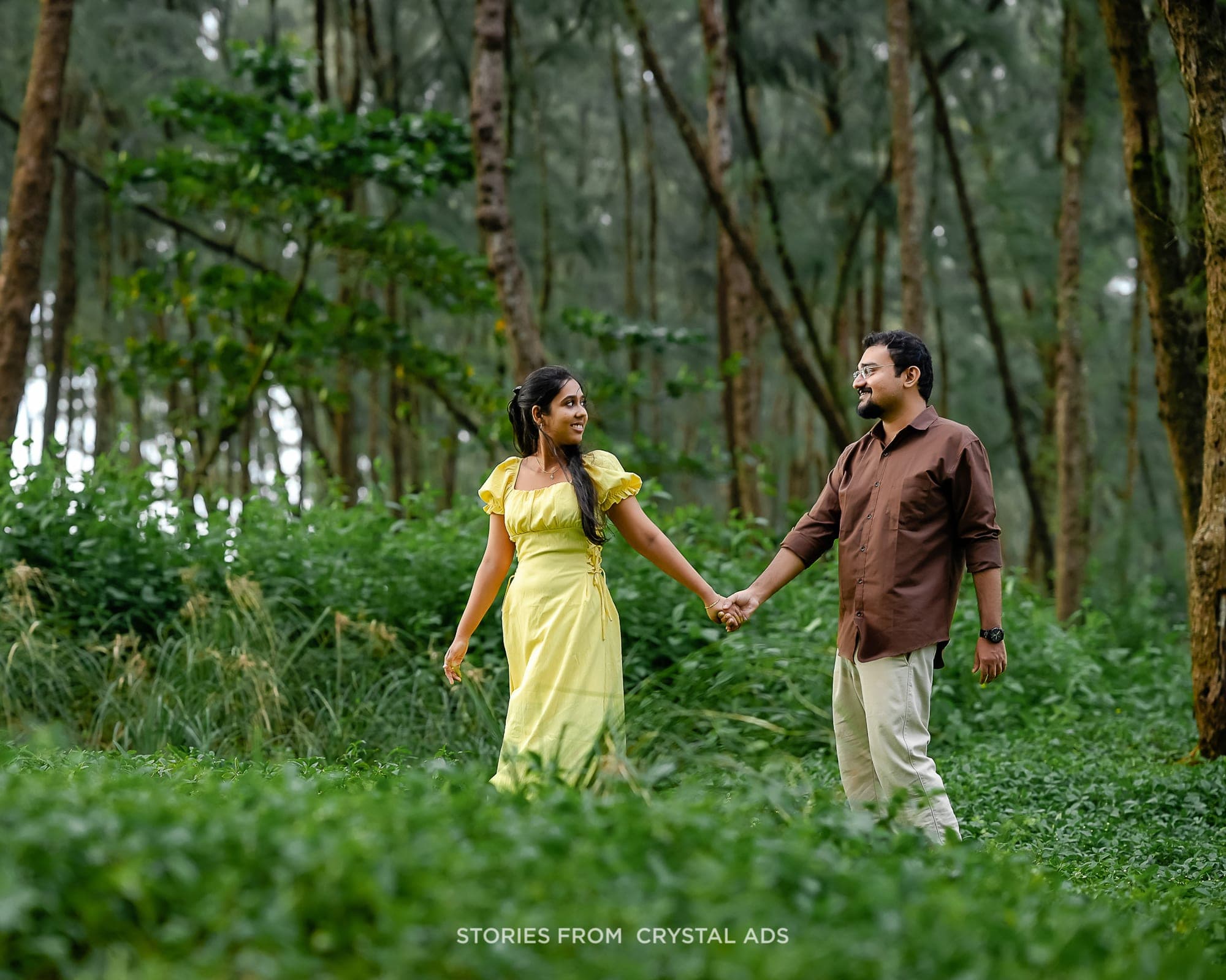 Couple holding hands as they walk through forest greenery